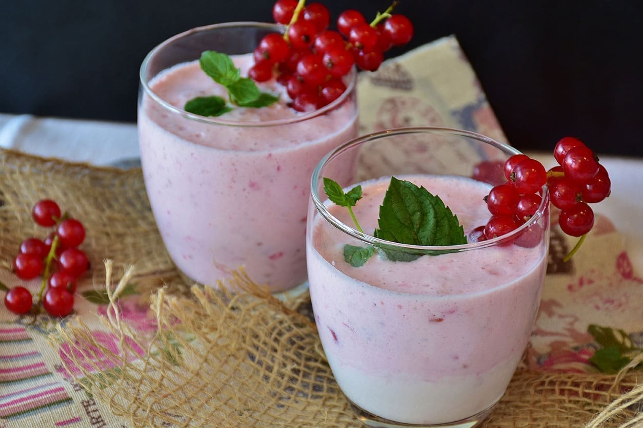 Two glasses of milk with red berries on top.